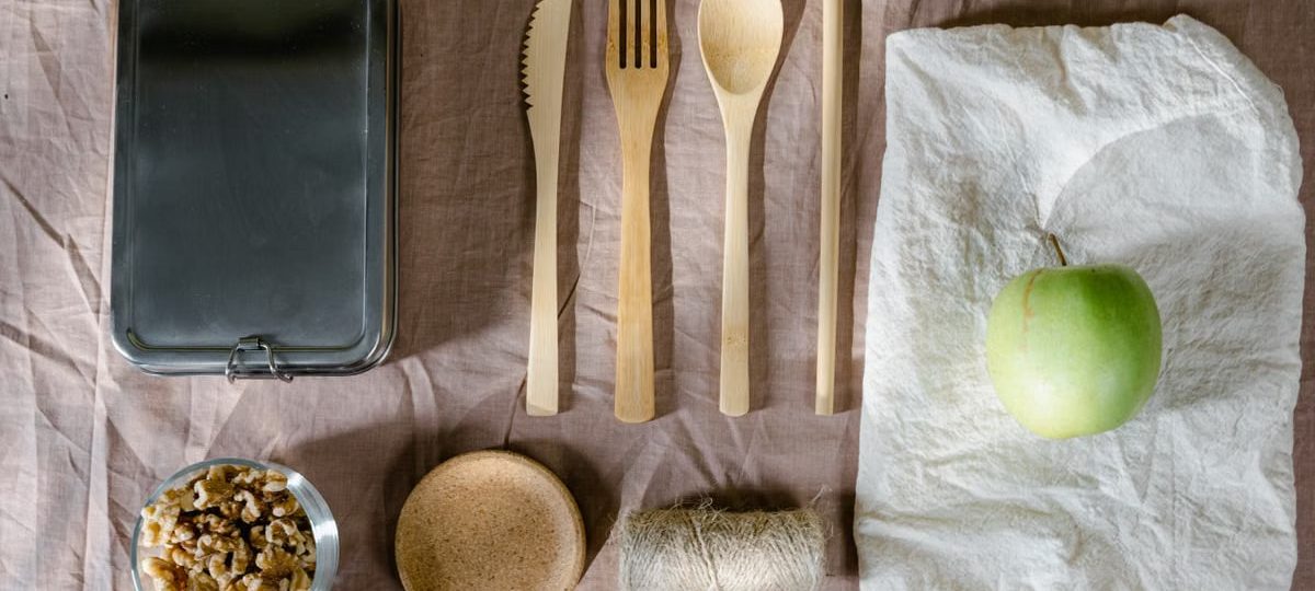 A flat lay of eco-friendly lunch items including wooden cutlery and a green apple.