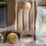 A flat lay of eco-friendly lunch items including wooden cutlery and a green apple.
