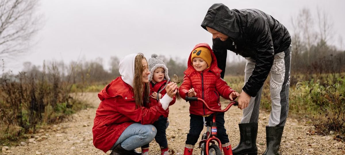 Happy family outdoors with children on a dirt path. Parents supporting kids on a bike ride.