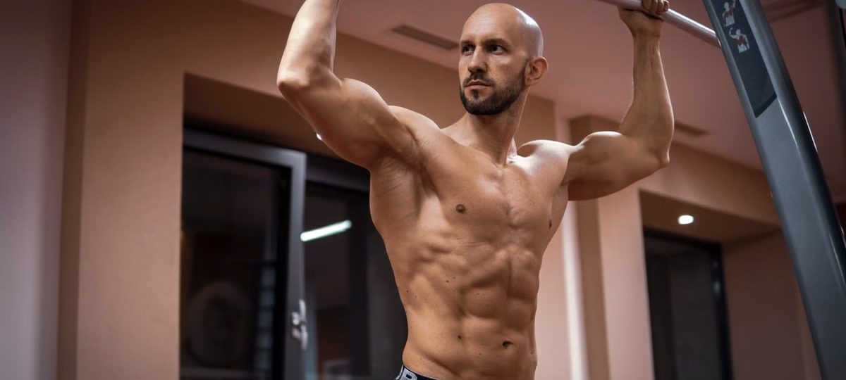 A bald, muscular man performing exercise on gym equipment indoors.