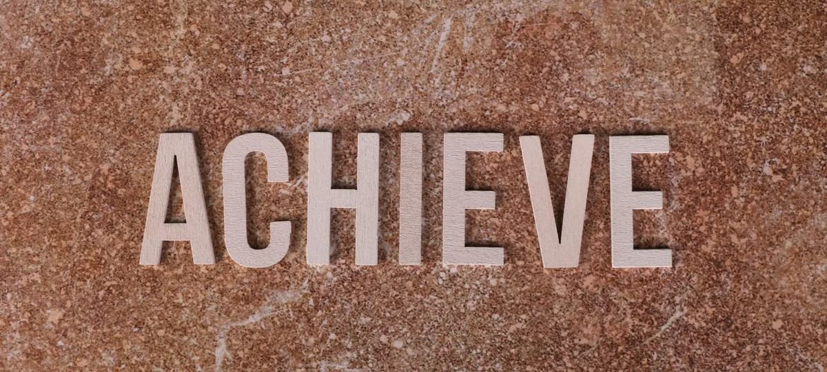 Wooden letters spelling 'ACHIEVE' on a textured brown surface, conveying motivation and success.